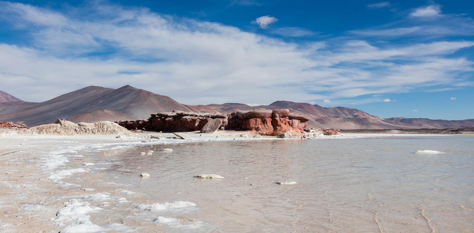 Red volcanic rock against the salt and water of the Salar de Aguas Calientes.
